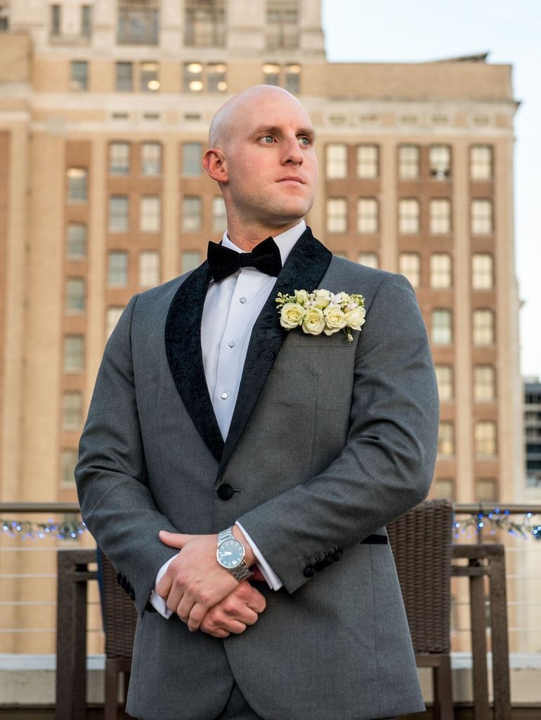 A man in a tuxedo and bow tie is standing in front of a building.