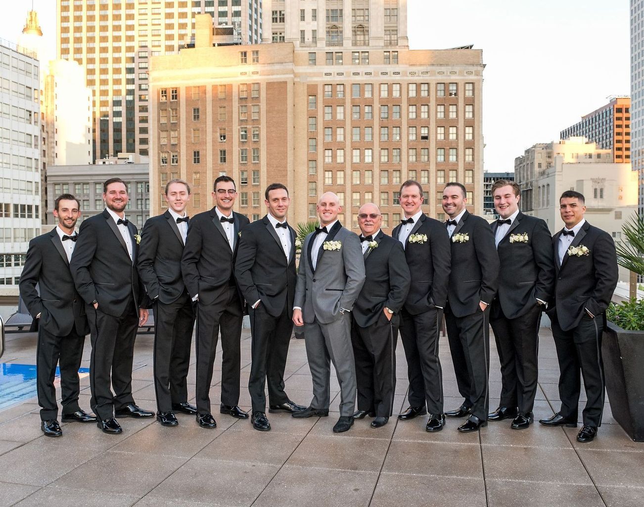 A group of men in tuxedos are posing for a picture on a rooftop.