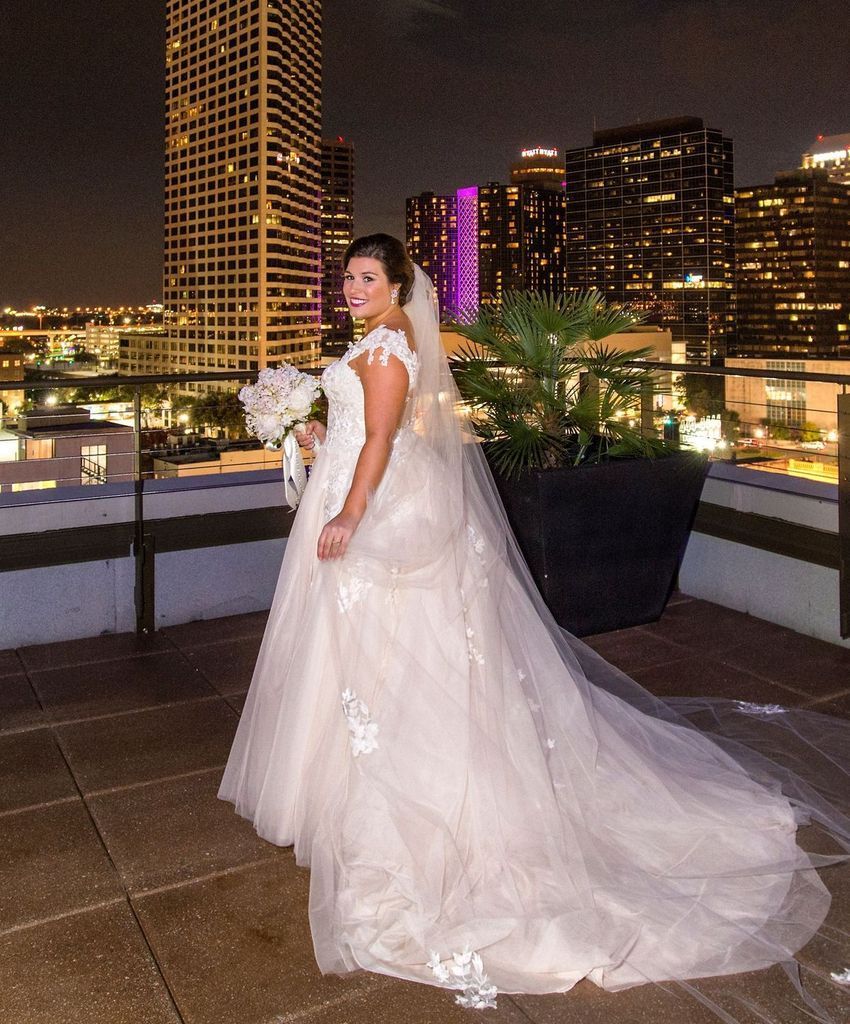 A bride in a wedding dress is standing in front of a city skyline at night.