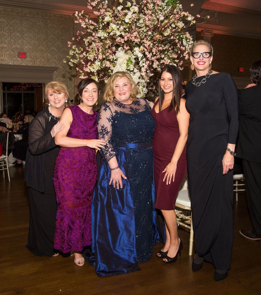 A group of women are posing for a picture in front of a flower arrangement.