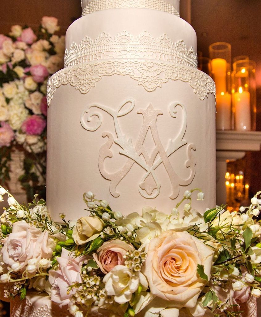 A wedding cake with a monogram on it is surrounded by flowers and candles