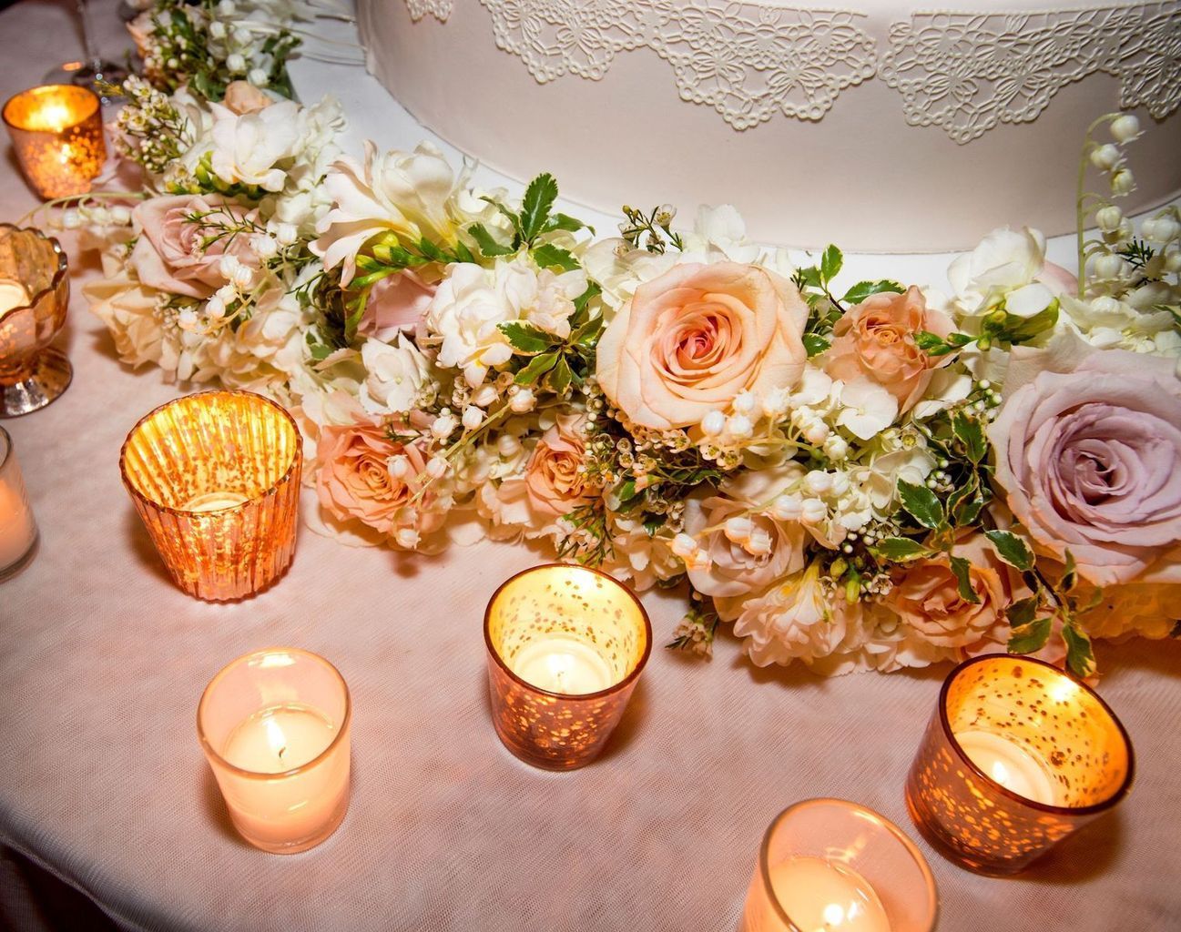 A wedding cake is surrounded by flowers and candles on a table.
