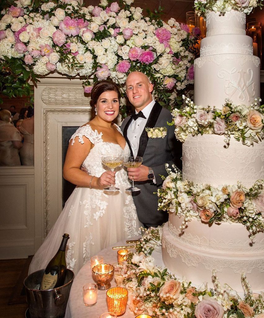A bride and groom are standing in front of a wedding cake.
