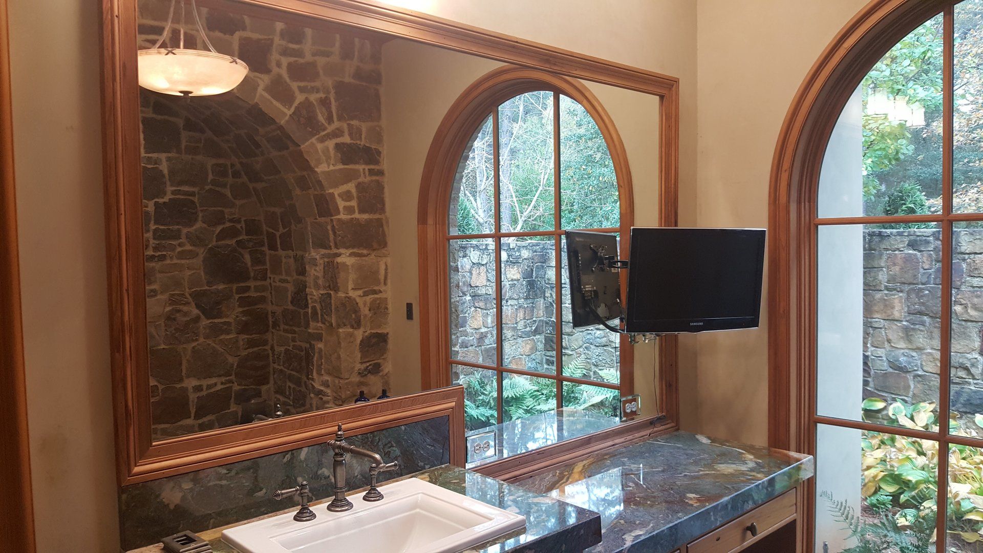 A bathroom with a sink , mirror and television.