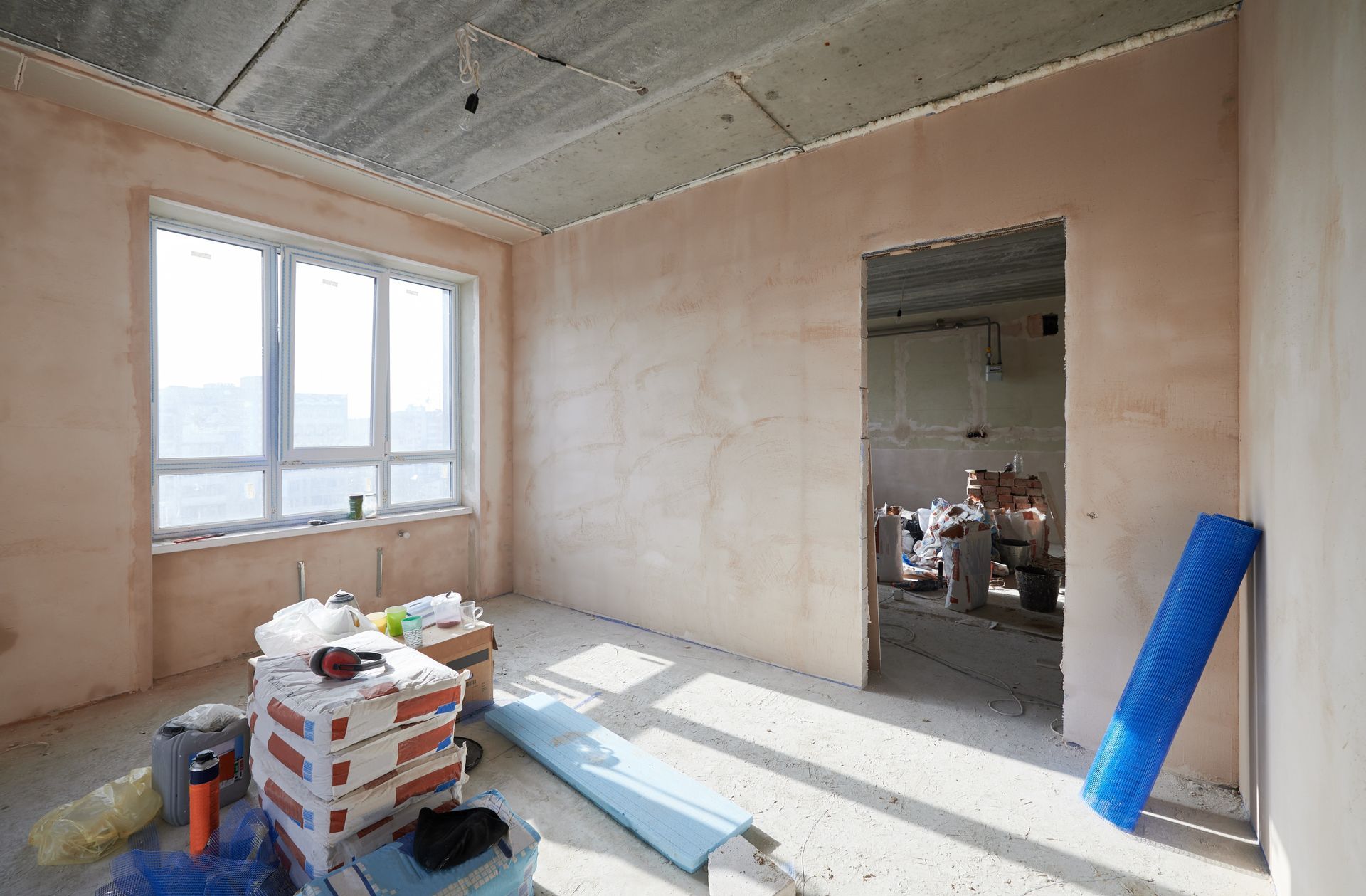 Room under construction, interior with window, doorway. Red brick, blue mat, and construction debris visible.