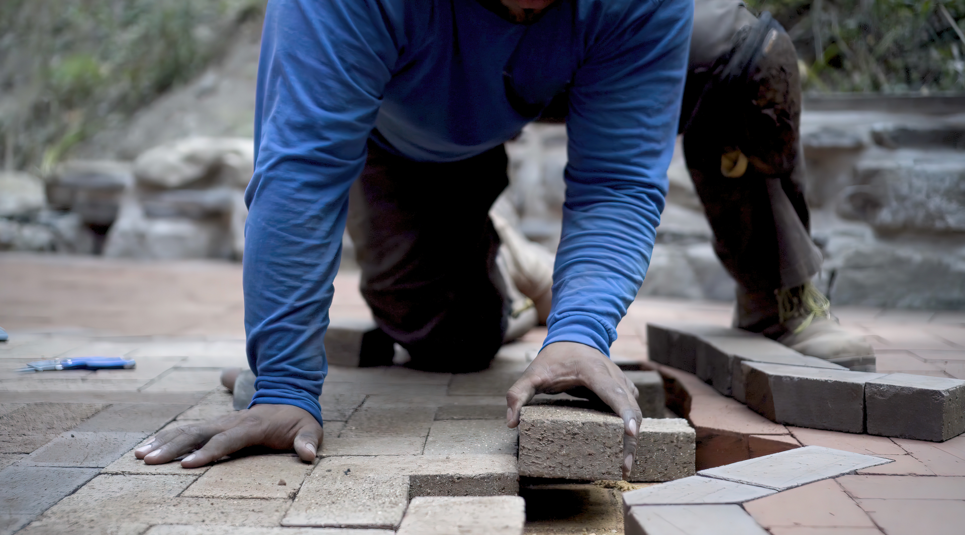 A man is laying bricks on a patio.