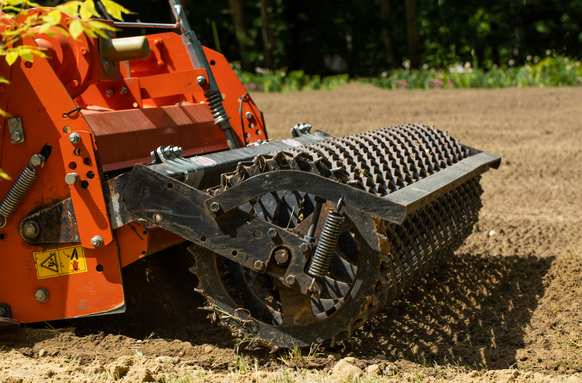 An orange and black machine is plowing a field.