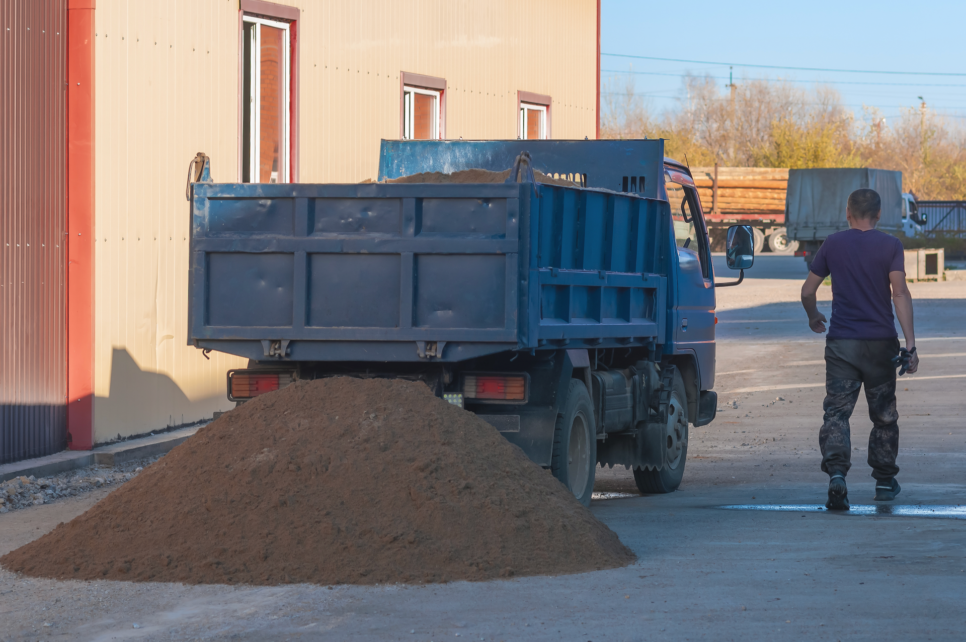 A man is standing in front of a dump truck filled with dirt.