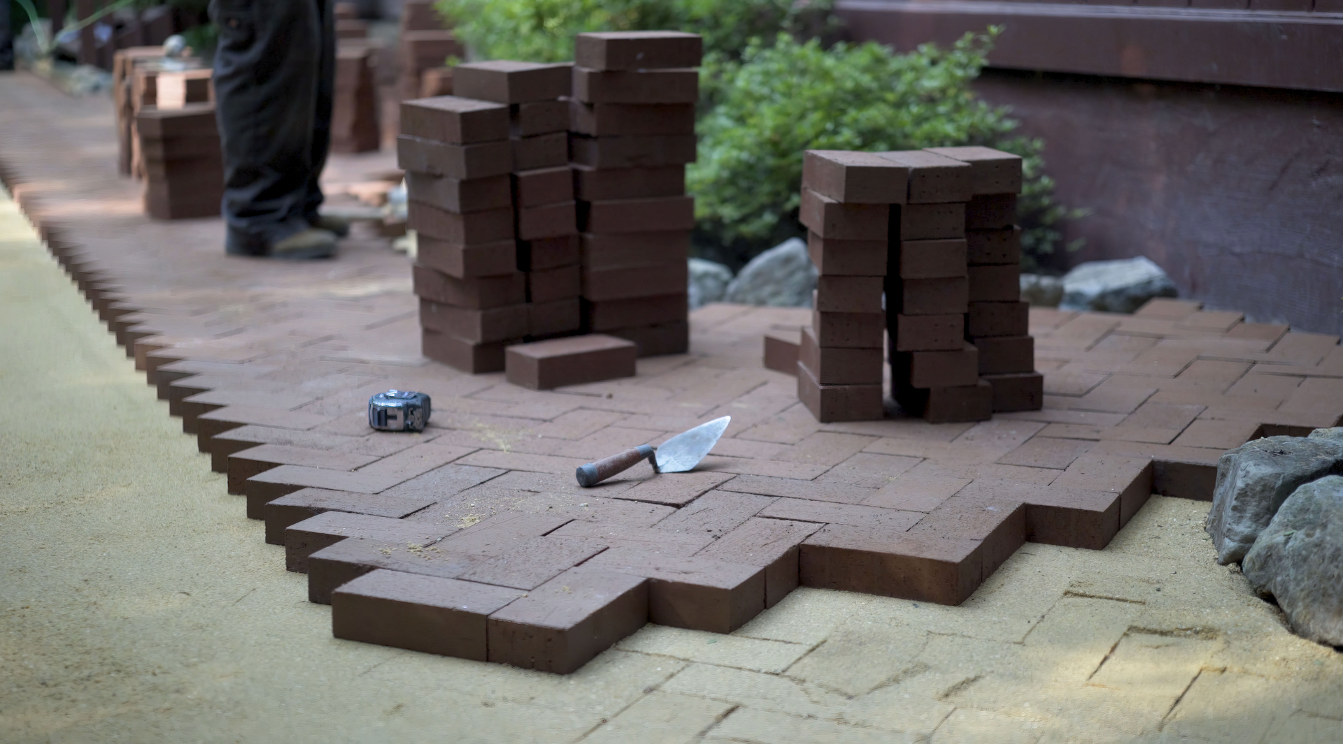 A brick walkway is being built with bricks and a trowel.