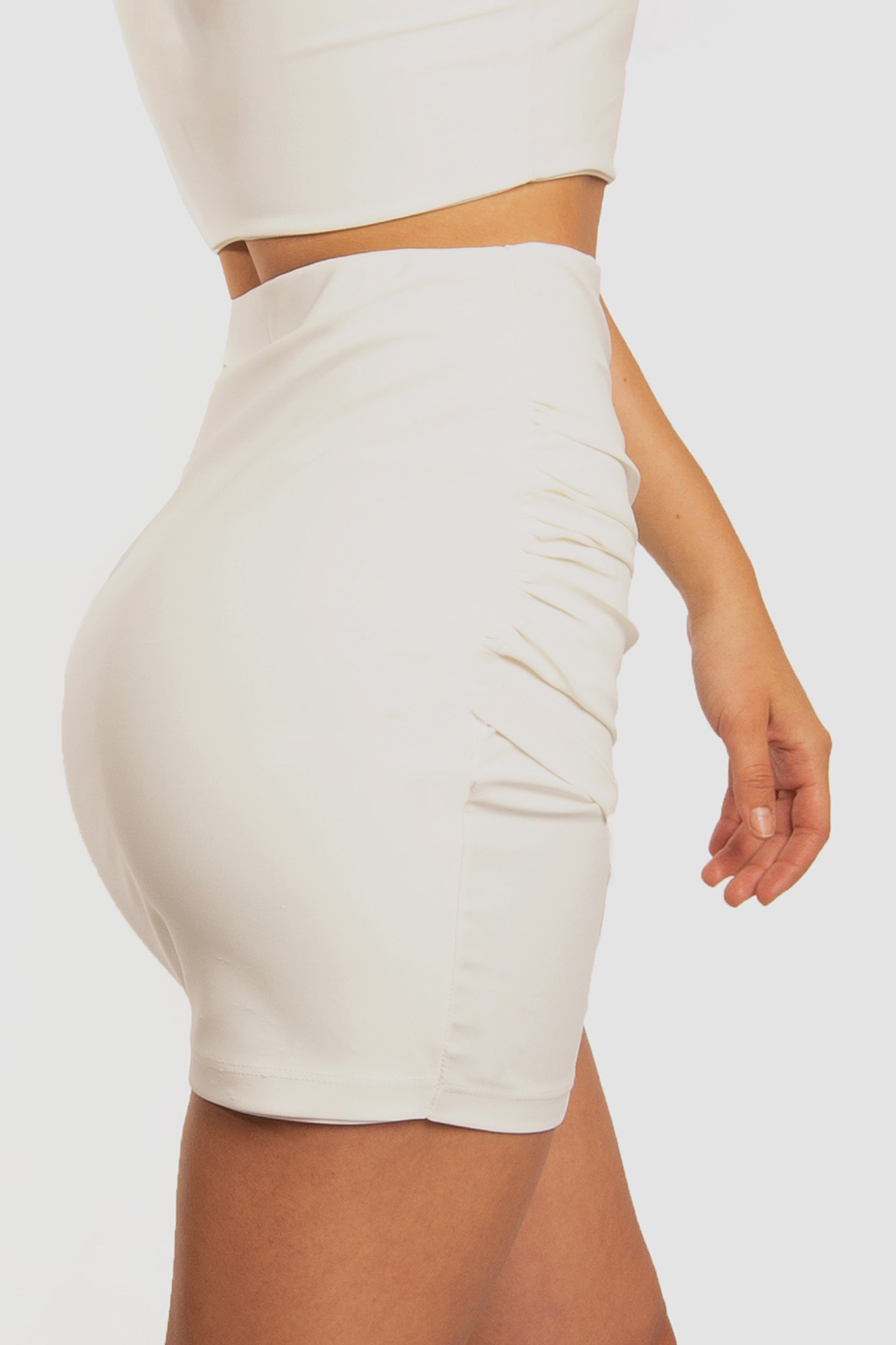 A woman is wearing a white crop top and a white skirt