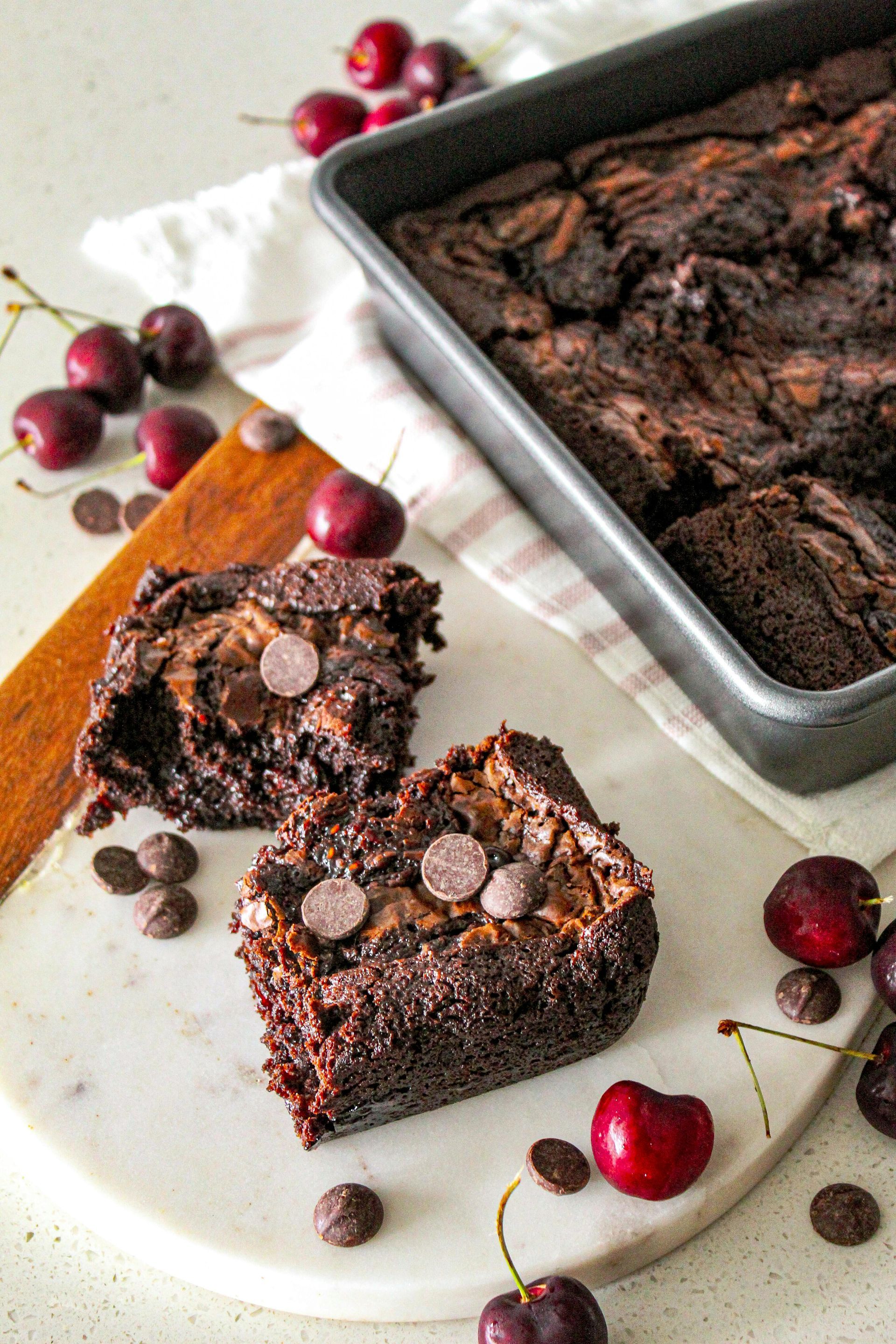 Chocolate brownies in a pan and cut, with cherries and chocolate chips.