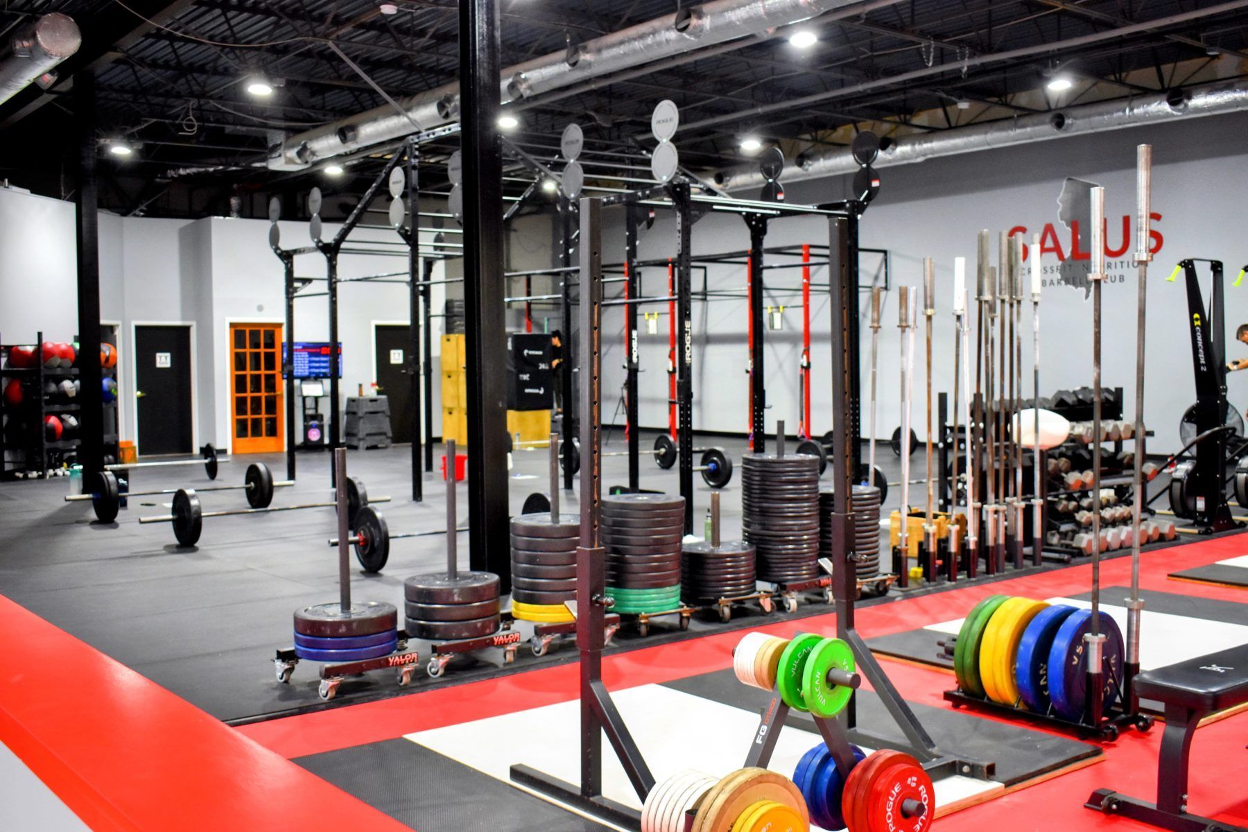 Weightlifting gym with racks, weights, and equipment. Red and black flooring.