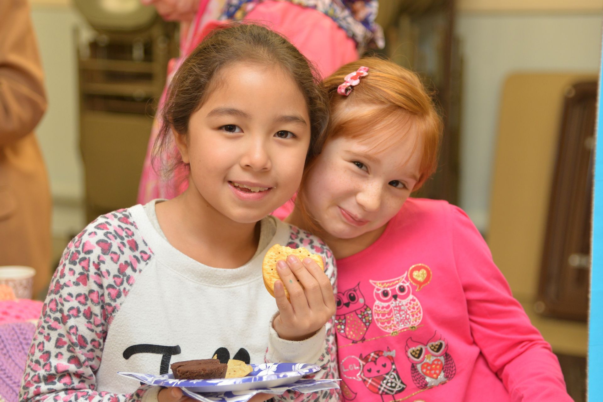 Two young girls are sitting next to each other eating cookies.