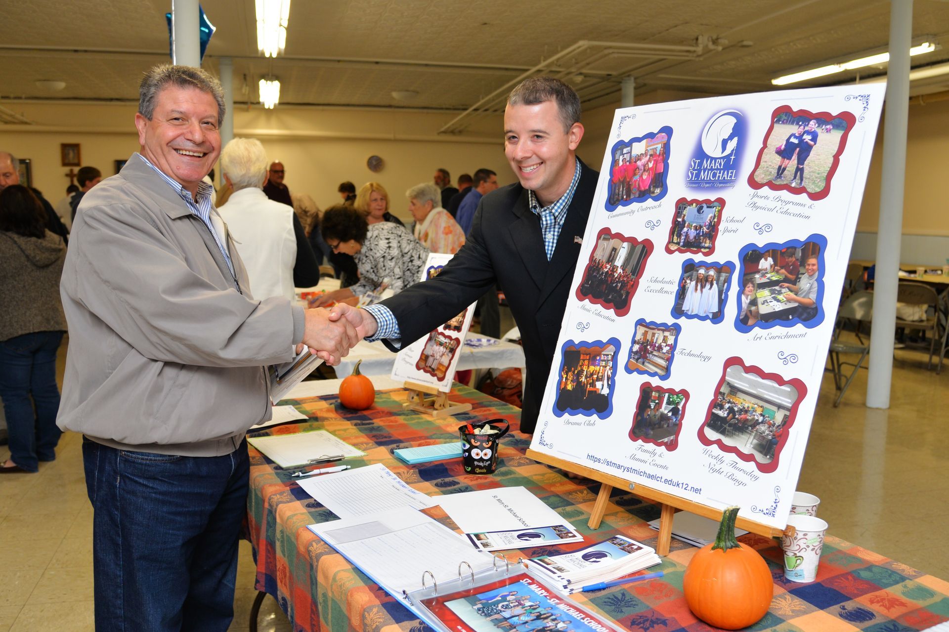 Two men shaking hands in front of a table with pictures on it