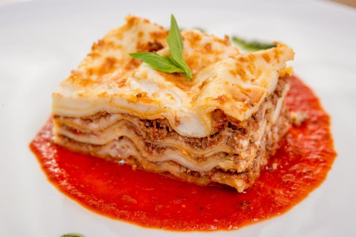 A slice of lasagna with tomato sauce on a white plate.