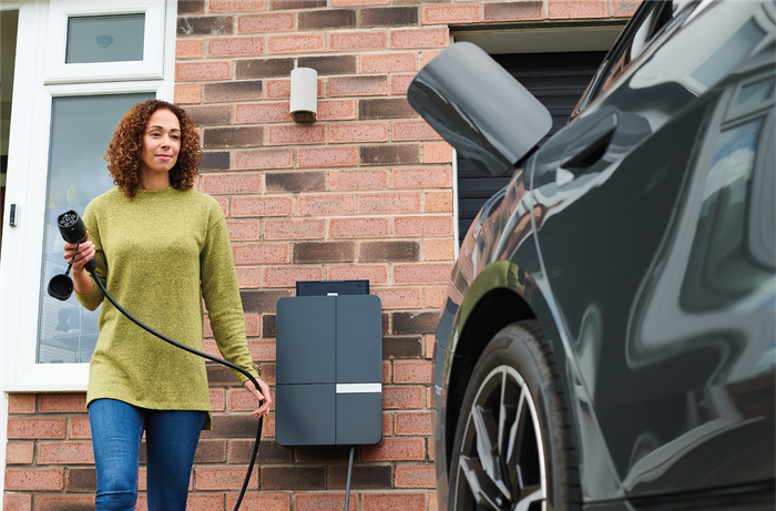 A woman is charging her electric car in front of her house.