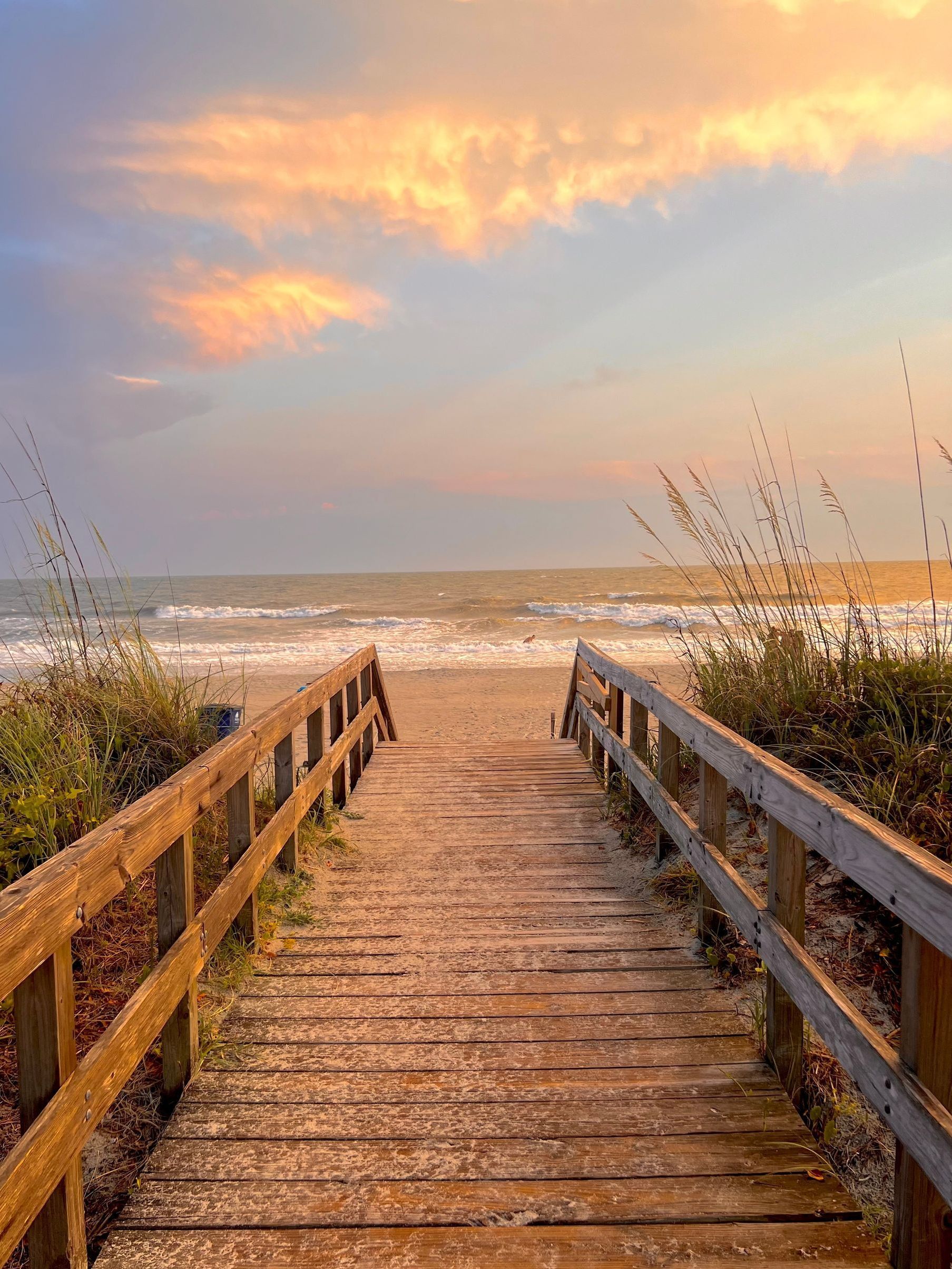 A wooden walkway leading to a gazebo overlooking a body of water at sunset.