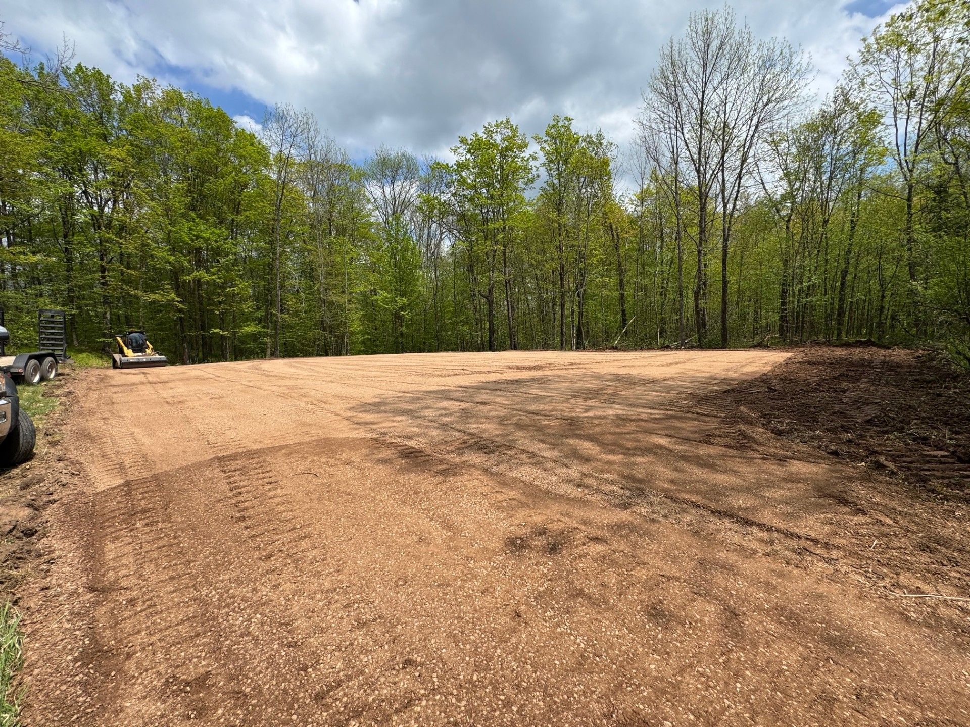 Cleared land area with wood chips, backed by forest and cloudy sky.