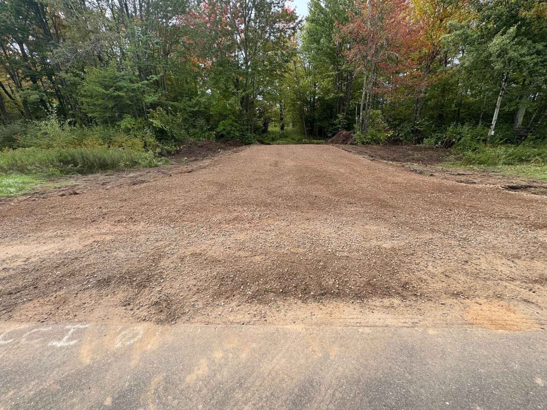 Brown gravel pile on paved road, leading to a tree-lined area.
