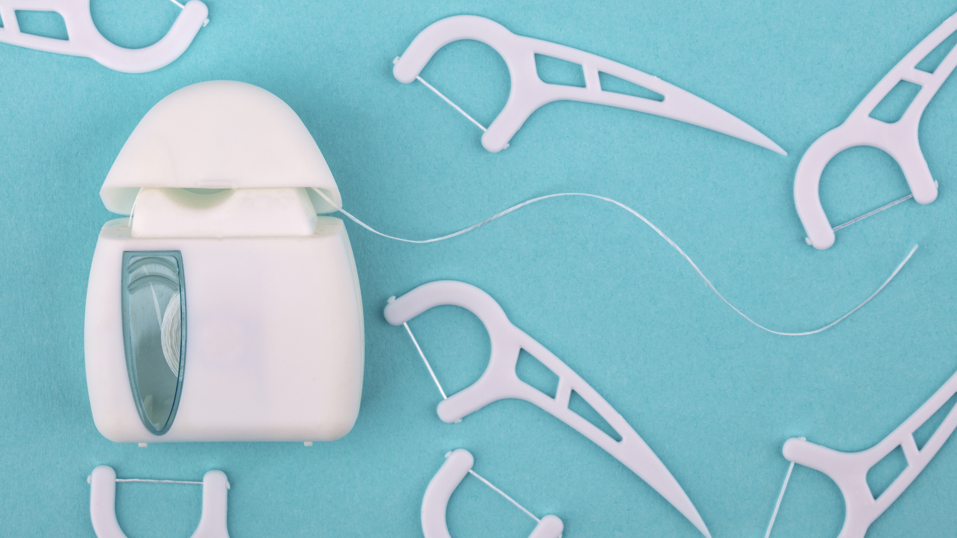 White dental floss container on a blue background with scattered floss picks