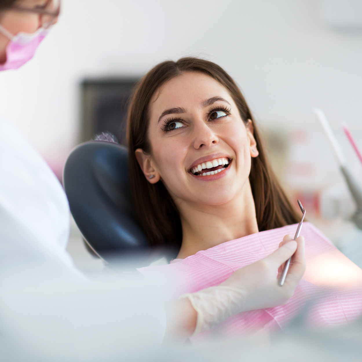 Smiling patient in a dental chair during a checkup, with a dentist nearby holding a tool