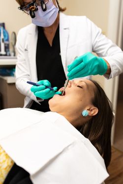 Dentist in white coat and green gloves examining a patient lying back in a dental chair