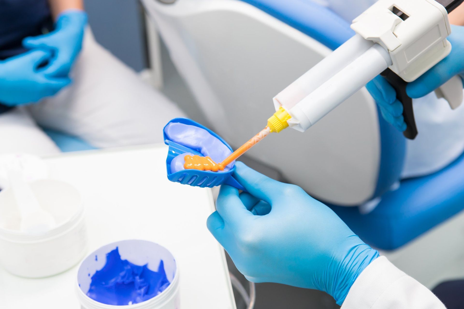 Dental tool applying blue composite to a tooth model with gloved hands in a clinic setting