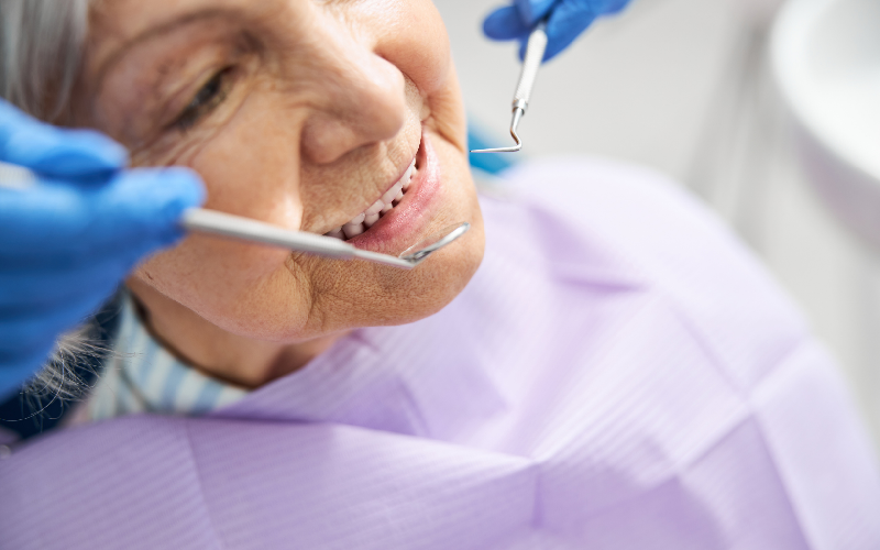 Smiling dental patient in a blue bib, with a dentist in blue gloves blurred in the background