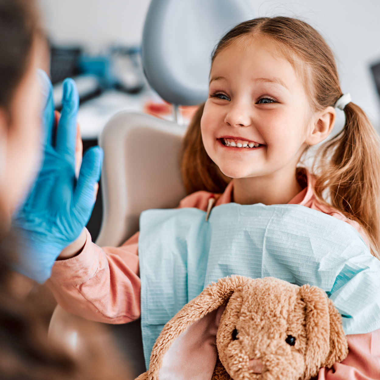 Smiling child in a dental chair giving two thumbs up, with a blue bib and white clinic background