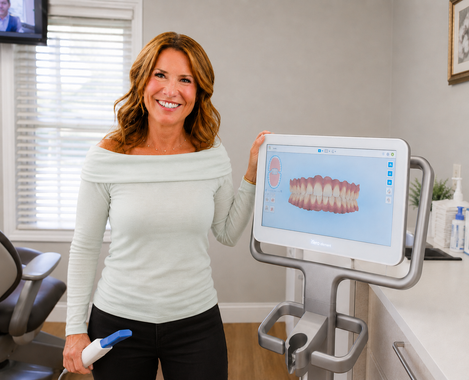 Woman smiling beside dental scanner displaying teeth model in a clinic room