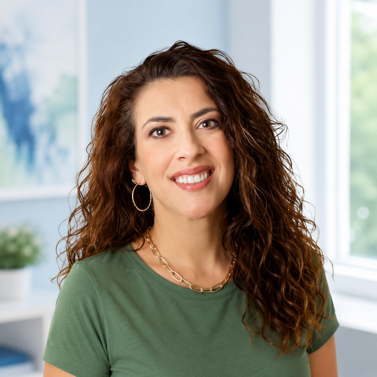 Smiling woman with curly hair in a green top, seated in a bright office setting