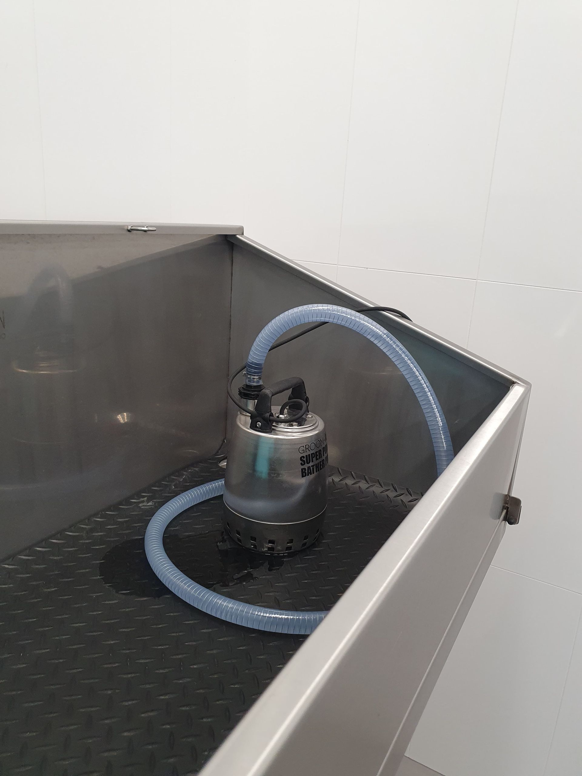 Roestvrijstalen container met pomp en slangen erin; witte achtergrond.