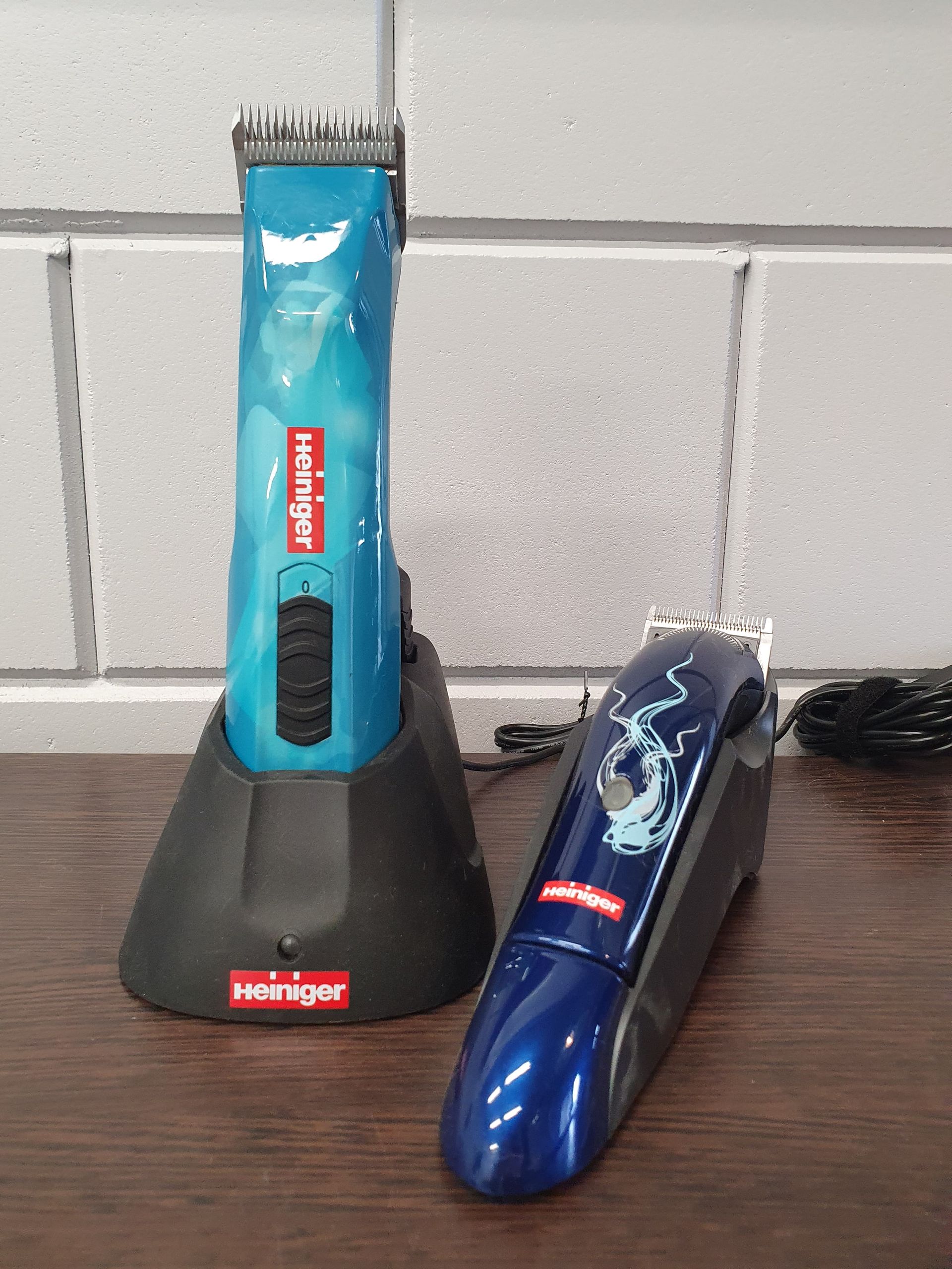 Twee blauwe tondeuses voor dieren met een oplaadstation op een houten oppervlak.