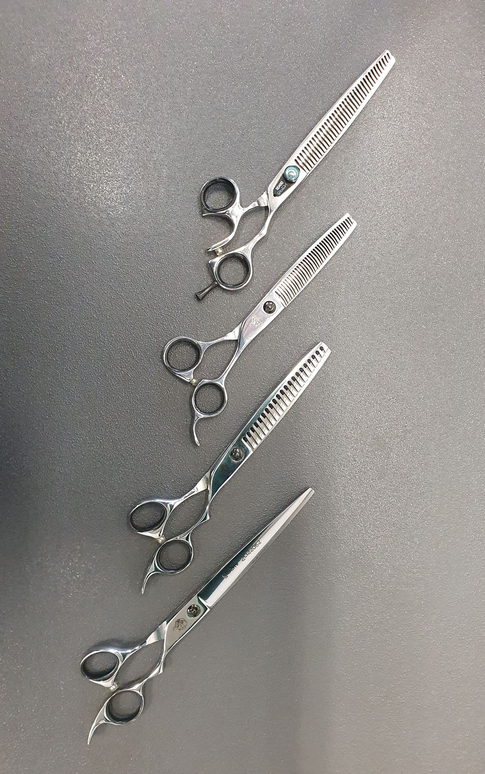 Zeven paar scharen voor het verzorgen van huisdieren liggen op een donkergrijs oppervlak.