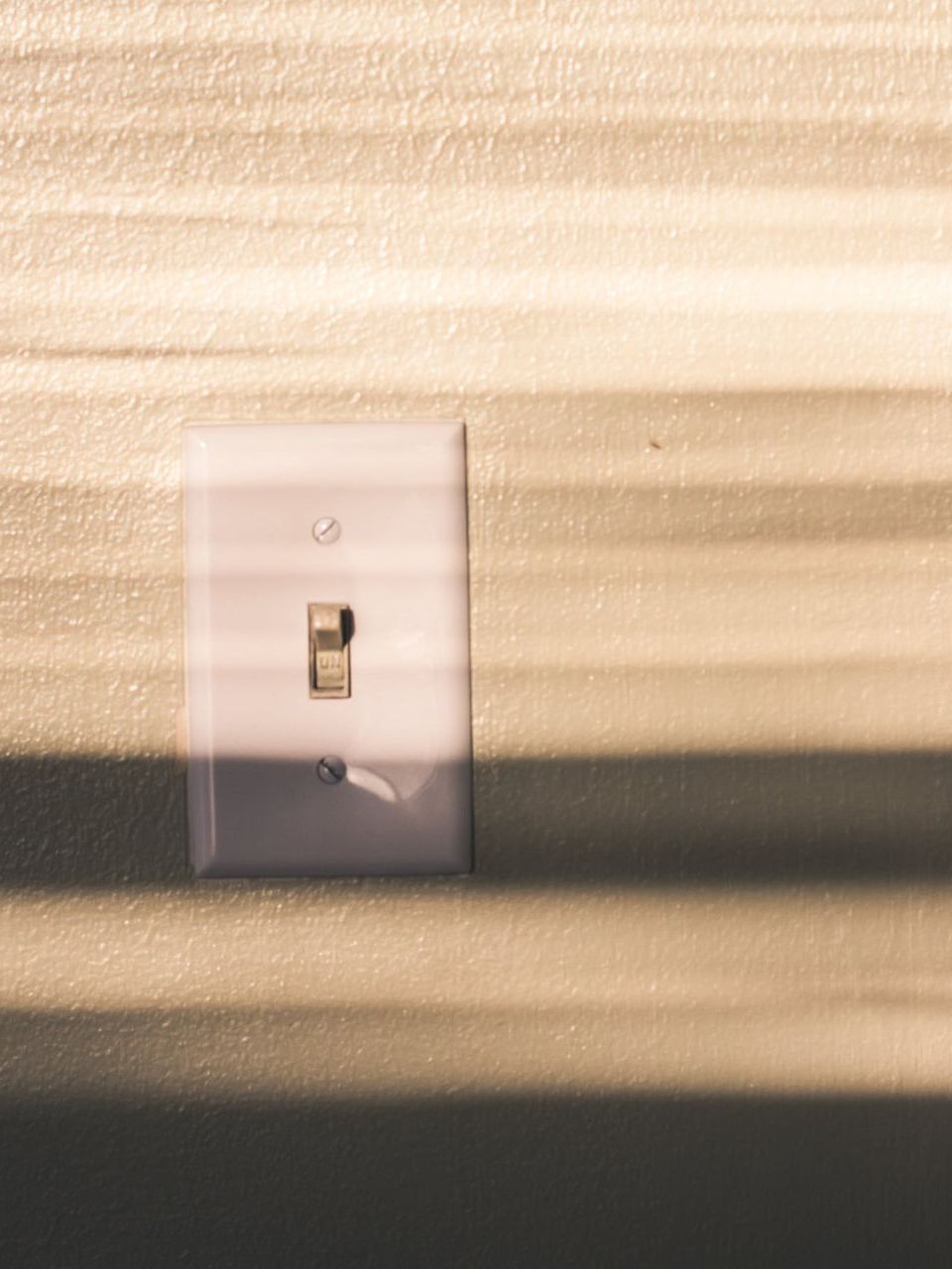 a light switch on a wall with a shadow on it .