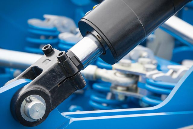 Black and silver hydraulic cylinder connected to blue machinery components.