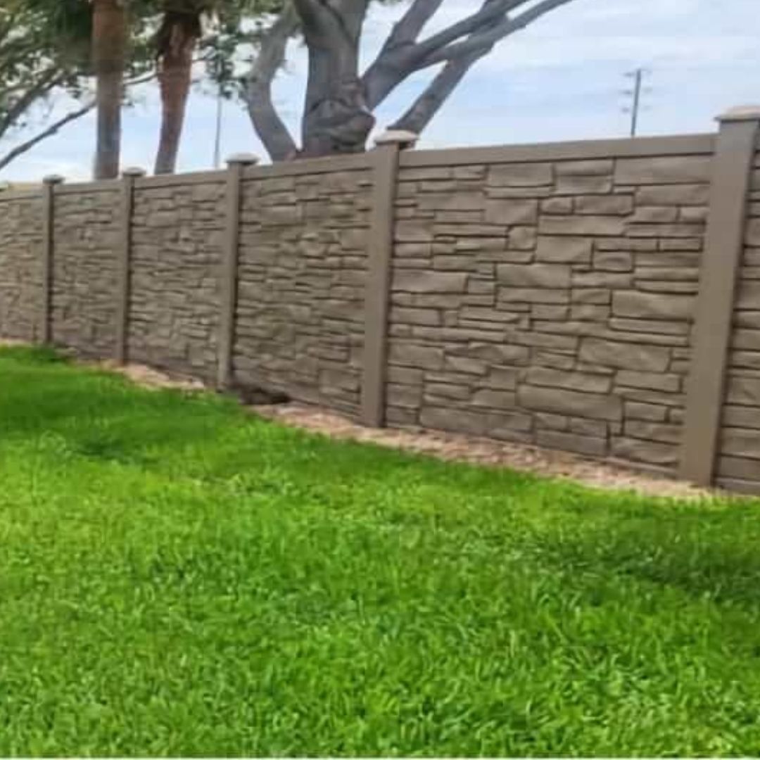 A stone fence surrounds a lush green field with trees in the background.