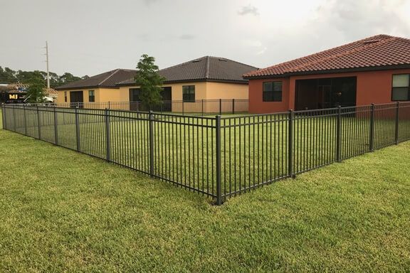 A fence surrounds a lush green yard in front of a house.
