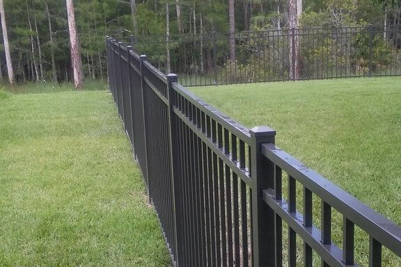 A black metal fence surrounds a lush green field.