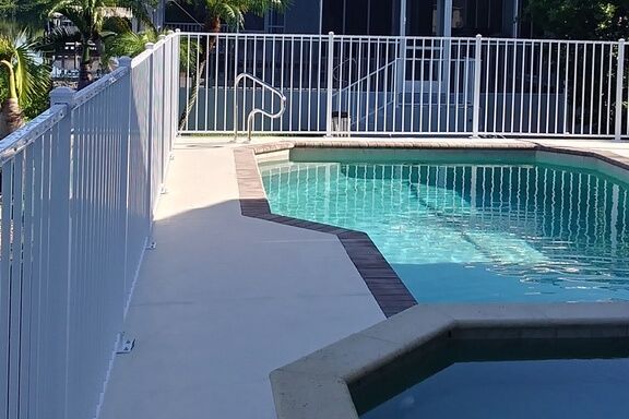 A large swimming pool surrounded by a white fence and a hot tub.