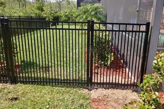 A black metal fence surrounds a lush green yard.