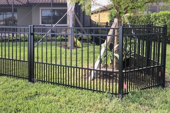 A black fence surrounds a lush green yard in front of a house.