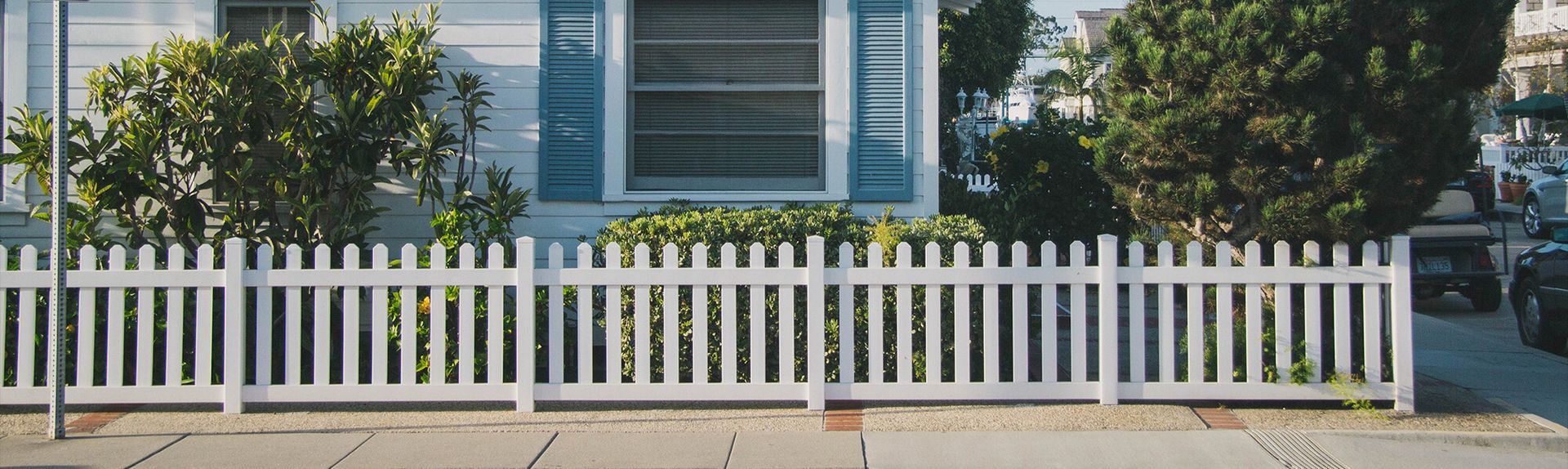 A white picket fence is in front of a white house.