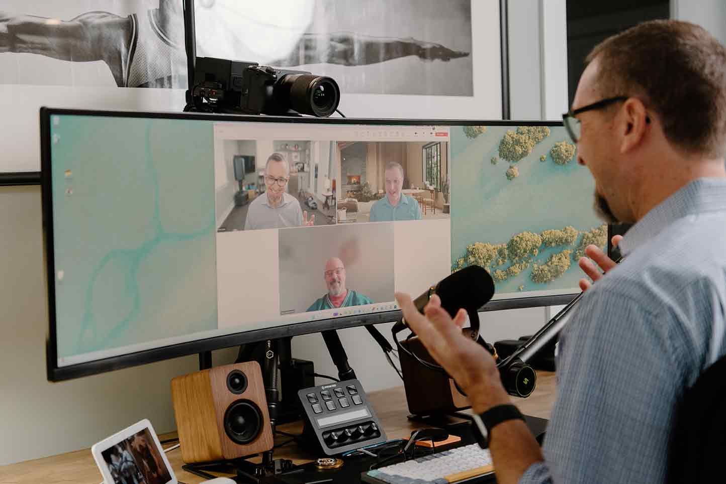 A man is sitting at a desk talking into a microphone while looking at a computer screen.