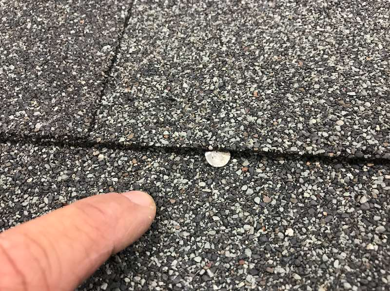 a person is pointing at a hole in a roof shingle .
