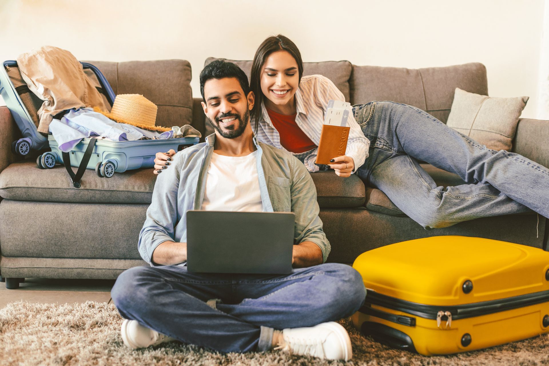 Couple relaxing on a couch with a laptop and drinks, with packed suitcases nearby