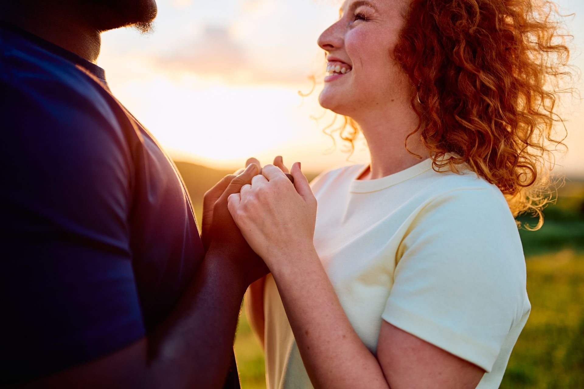 Two people holding hands and smiling at sunset in a grassy field