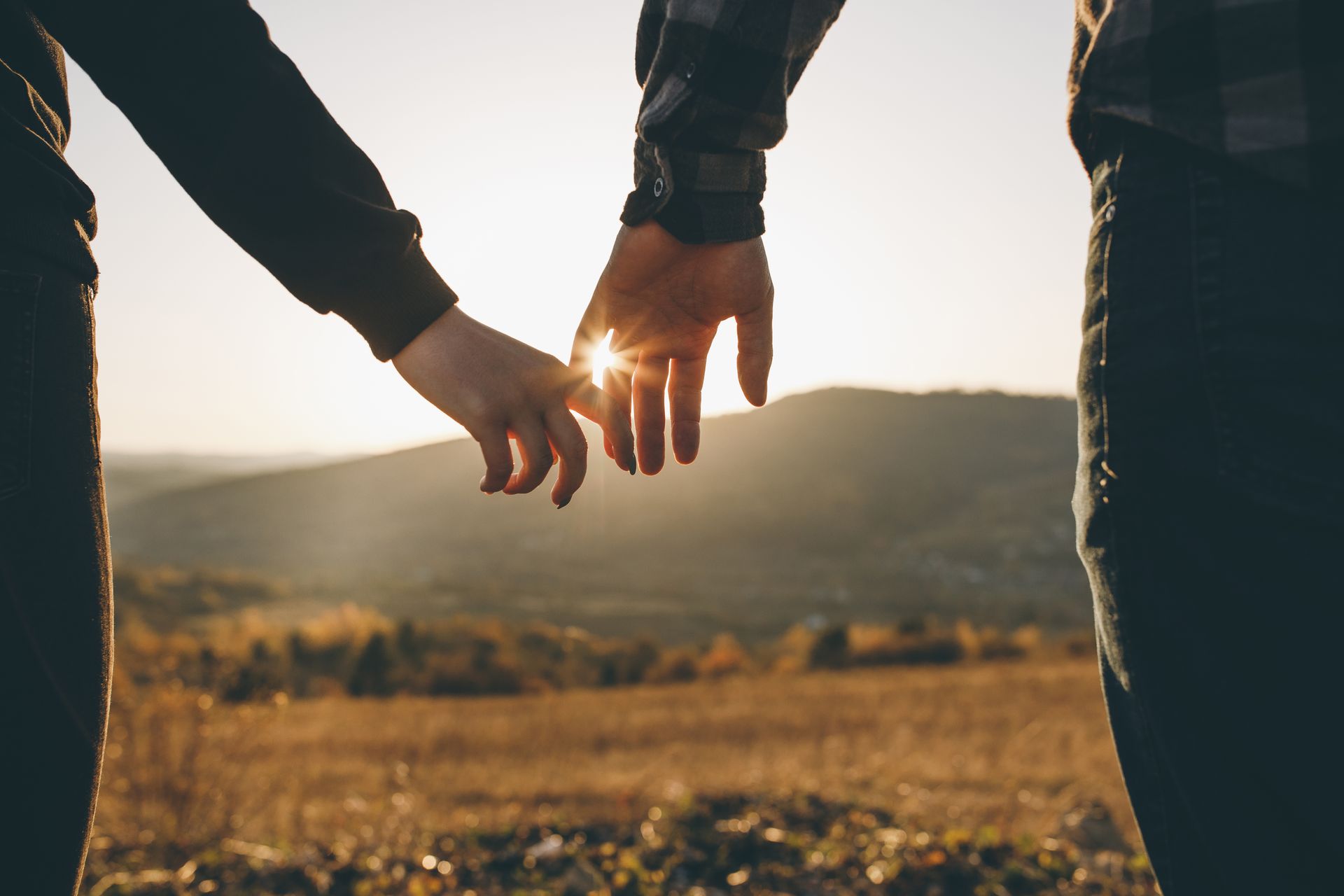 Two people holding hands at sunset in a field, with warm light between their fingers