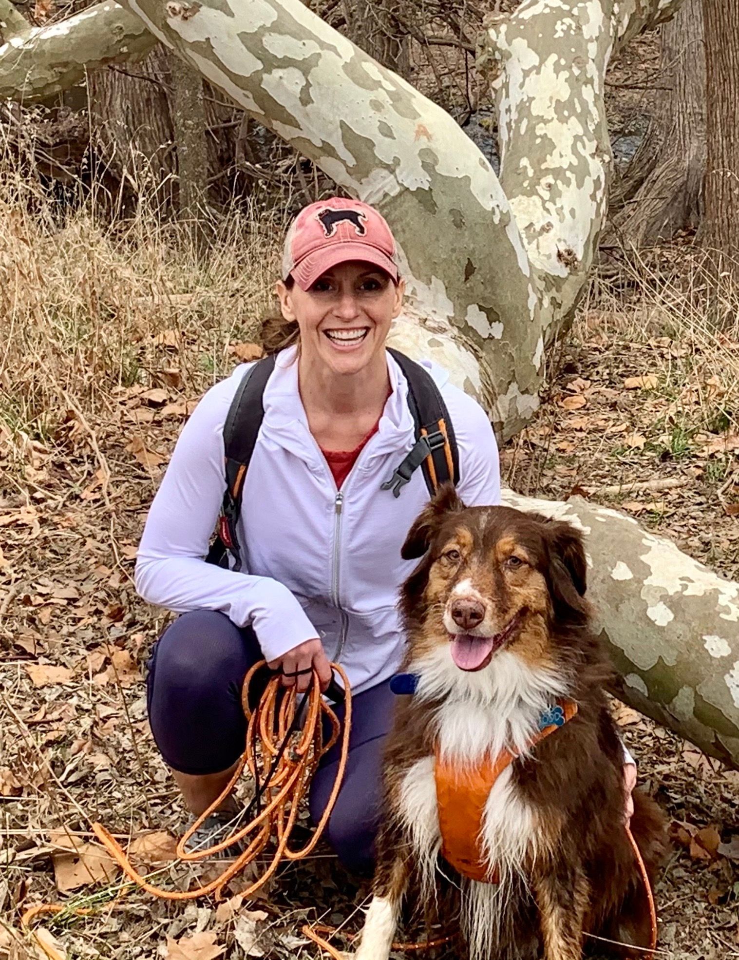 A dog trainer is kneeling down next to a dog on a leash.
