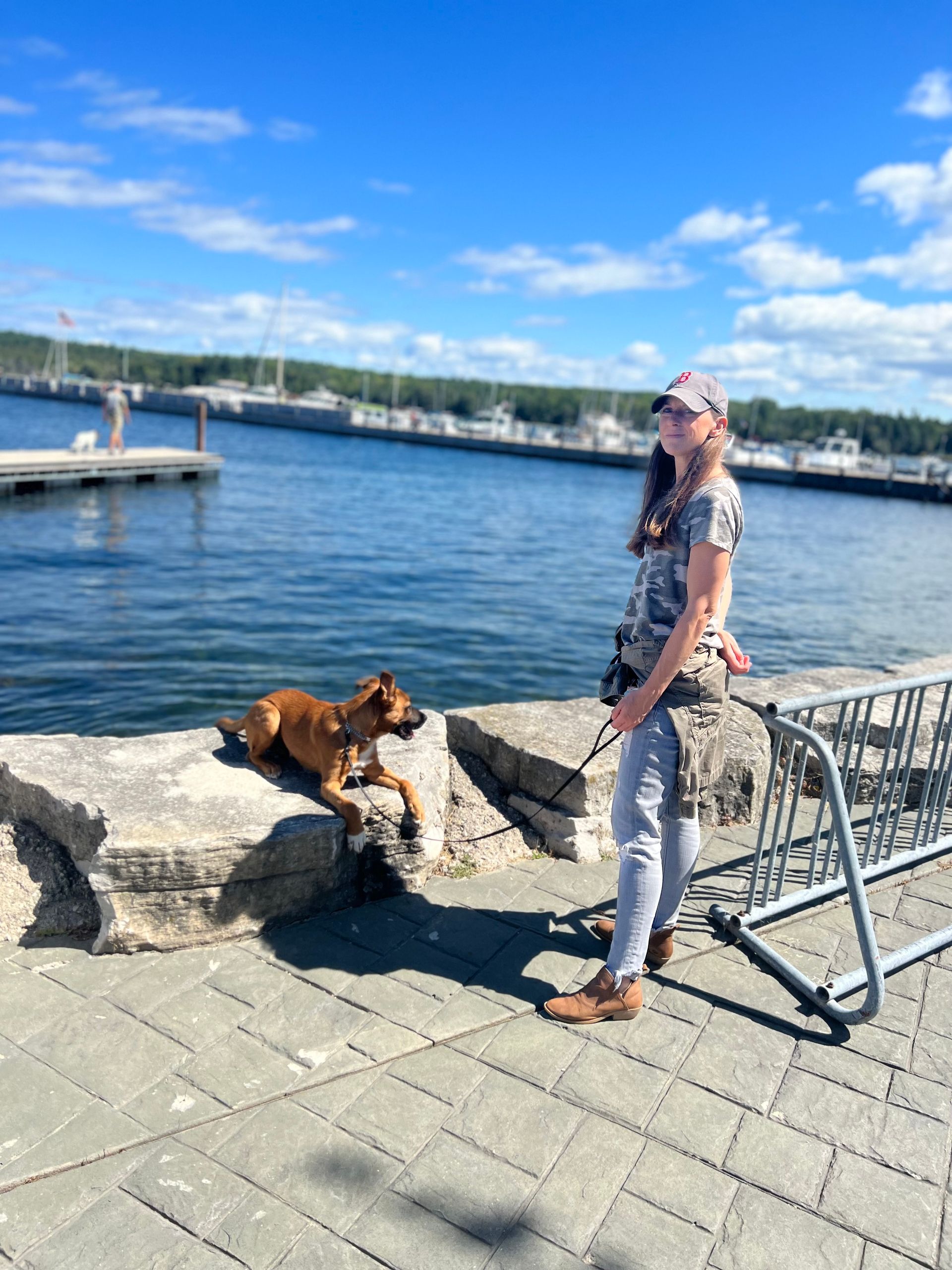 A dog trainer is standing next to a dog on a leash by the water.